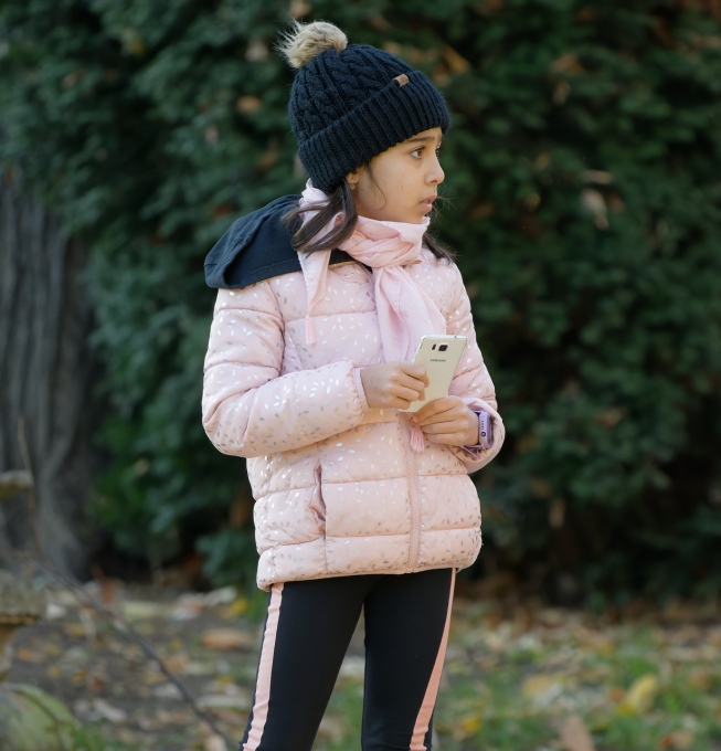 Dziewczynka w zimowym ubraniu trzyma w dłoniach smartfon.